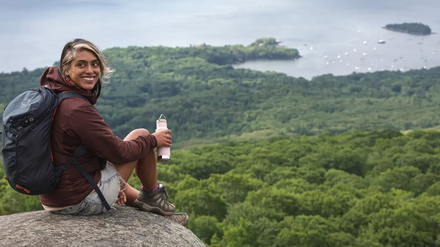 Smiling woman sitting on a rock above a forest and a lake.